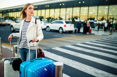 Stunning blonde lady with blue and white suitcases stands before crossing on the street