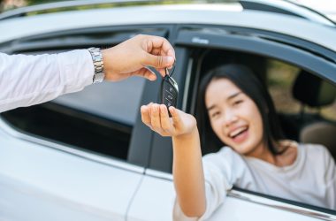 A woman sits in a car and holds out her hand to receive the car keys.